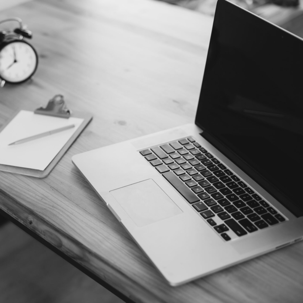 Ein Laptop der auf einen Tisch steht, neben dem Laptop liegen Blätter - Unterlagen.